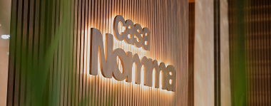 Logo da Casa Nomma retroiluminado em painel ripado de madeira.