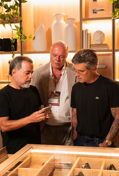 Três homens observam um produto da Nomma na Casa Nomma, com Duda Porto e Bruno Gagliasso examinando os detalhes.