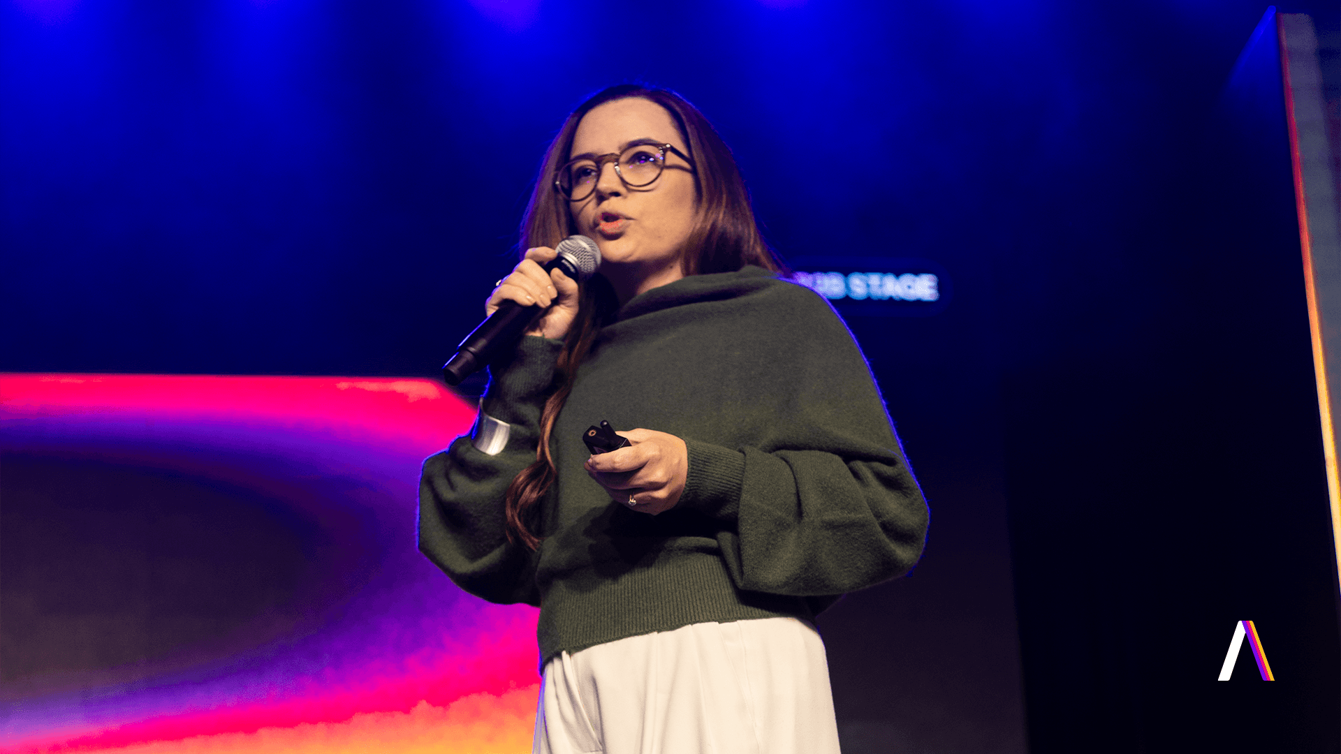 B2B Summit 2026: Samira Cardoso, CEO da Layer Up, discursa ao microfone no palco principal do evento, com iluminação azul e rosa ao fundo